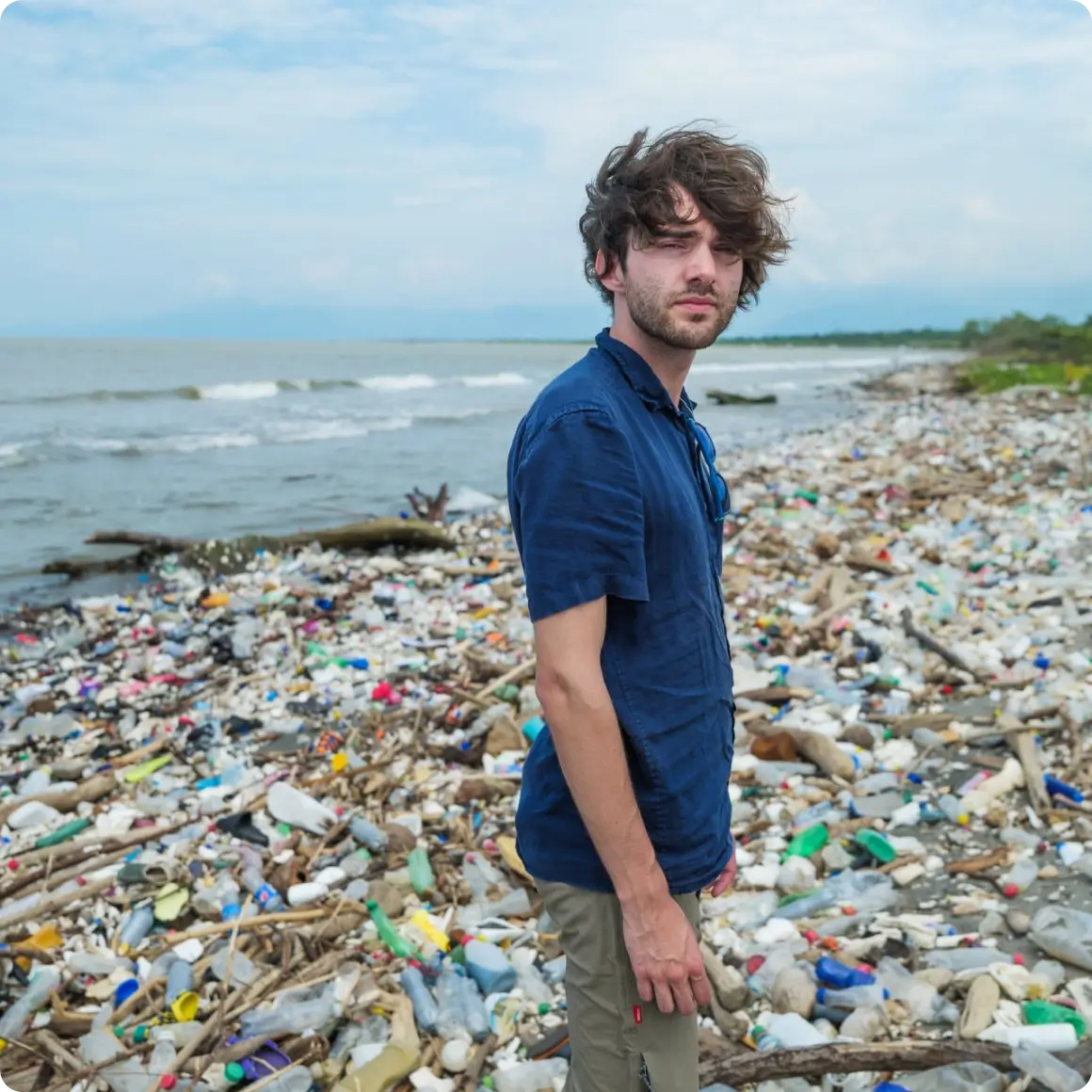 Man standing on a beach covered in plastic waste.